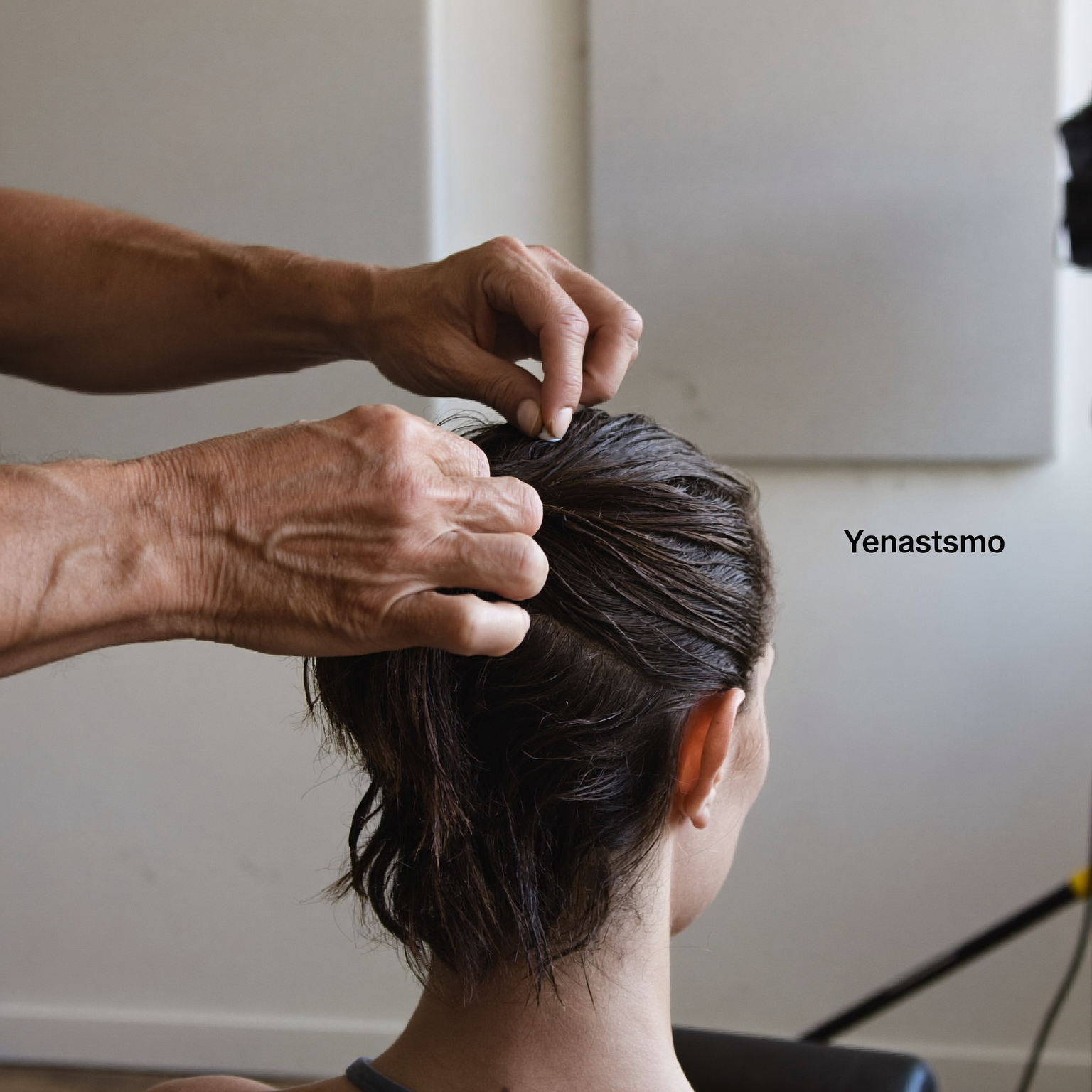 Practitioner's hands parting dry hair while preparing a small scalp sensor in a quiet studio room